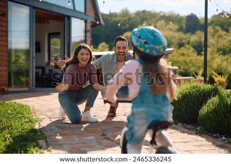 Cheerful parents encouraging their daughter in riding bicycle outdoors.
