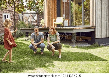 Cheerful parents looking at daughter while crouching on grassy land in yard