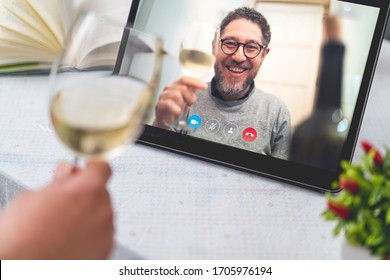 Cheerful people celebrating friendship toasting online during a remote video call - close up of a tablet displaying a mid aged man raising white wine glass. - Powered by Shutterstock