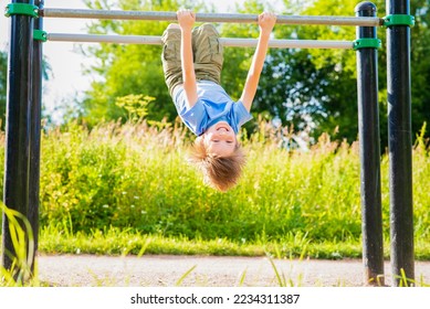 cheerful perky boy hangs, plays on uneven bars in the summer in the park - Shutterstock ID 2234311387