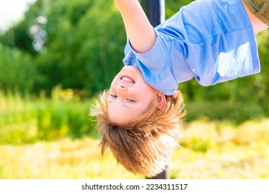cheerful perky boy hangs, plays on uneven bars in the summer in the park - Shutterstock ID 2234311517