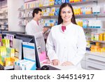 Cheerful pharmacist standing at pay desk and pharmacy technician helping 