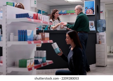 Cheerful Pharmacy Worker Discussing About Healthcare Treatment With Elderly Client, Explaining Pills Leaflet During Medical Consultation. Customer Buying Supplements, Vitamin To Cure Disease