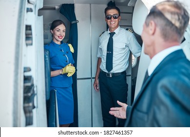 Cheerful pilot and stewardess are greeting elegant man on stairway while he is boarding before flight