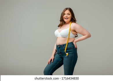 Cheerful Plus Size Woman In Jeans And Bra Standing With Hand On Hip Isolated On Grey