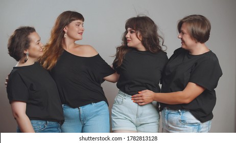 Cheerful Plus Size Women In Black T-shirts And Jeans Embracing And Smiling At Camera. Group Of Beautiful Overweight Ladies Posing Isolated On Grey Background. Body Positive Concept