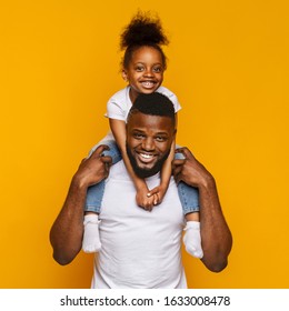 Cheerful Portrait Of Black Dad And Little Daughter Sitting On Father Shoulders Over Yellow Background