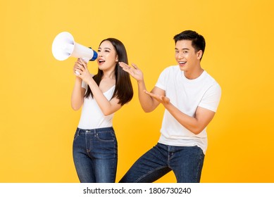 Cheerful Portrait Of Smiling Happy Young Asian Couple Making Announcement And Presenting In Isolated Studio Yellow Background