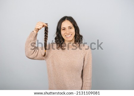 Cheerful portrait of a young girl holding a braid of hair to donate for wigs and cancer patients. Studio shot over grey background.