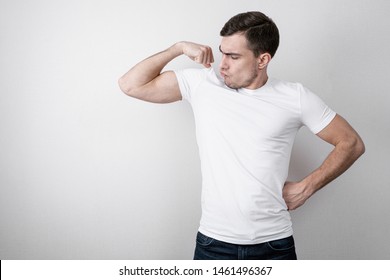 Cheerful portrait of young man in white blank t-shirt shows the biceps on gray background with copy space - Powered by Shutterstock