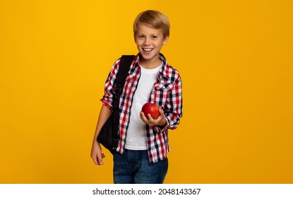 Cheerful Positive European Teenager Boy Pupil With Backpack Holding Red Apple And Ready To Study, Isolated On Yellow Background, Copy Space. Health Care, Proper Nutrition, Diet And Back To School