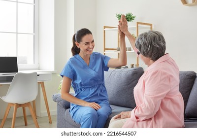 Cheerful positive female nurse giving high five to her senior female patient during visit. Caregiver is sitting on sofa with retired patient and congratulates her on successful outcome of treatment. - Powered by Shutterstock