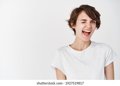 Cheerful and positive natural girl winking at camera, feeling motivated and happy, smiling on white background. - Shutterstock ID 1927519817