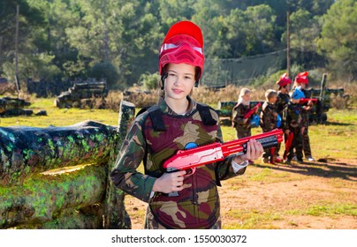 Cheerful Positive  Teen Girl Wearing Uniform And Holding Gun Ready For Playing With Friends On Paintball Outdoor