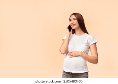 Cheerful Pregnant Girl Talking On Phone Consulting With Doctor Standing In Studio Over White Background. Empty Space - Powered by Shutterstock