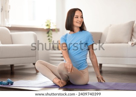 Cheerful pregnant lady doing seated rotation stretch, exercising on yoga mat having workout at home, sitting in living room during training. Healthy and sporty pregnancy