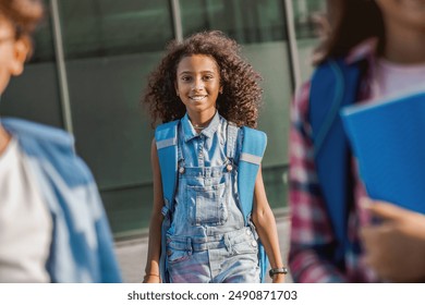 Cheerful preteen african child girl elementary middle school pupil with backpack going to school lessons home with fun smiling looking at the camera together with her friends classmates - Powered by Shutterstock