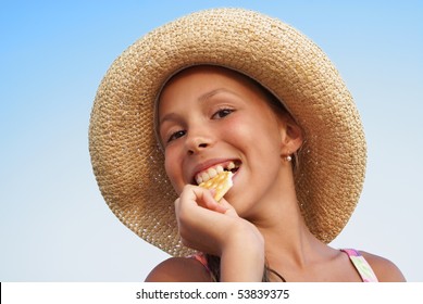 Cheerful preteen girl in straw hat eating cookie on blue sky background