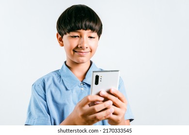 Cheerful Preteen Mix Race Boy Kid In A School Uniform Using A Smartphone For Online Learning, Social Media, Chat Texting Or Playing An Online Game On White Background. Child Technology Study Concept.