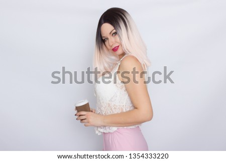 Cheerful pretty blonde woman in white shirt and pink pants with a cup of coffee over white background