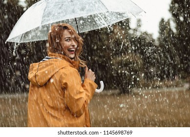 Cheerful pretty girl holding umbrella while strolling outside. She is turning back and looking at camera with true delight and sincere smile. Copy space in right side - Shutterstock ID 1145698769