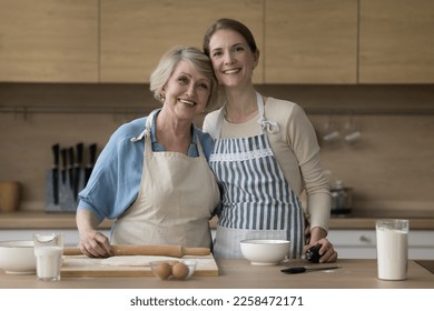 Cheerful pretty mature mother and adult daughter woman baking at kitchen table with bakery food ingredients, flour, eggs, holding roller, looking at camera, hugging, smiling. Home portrait - Powered by Shutterstock