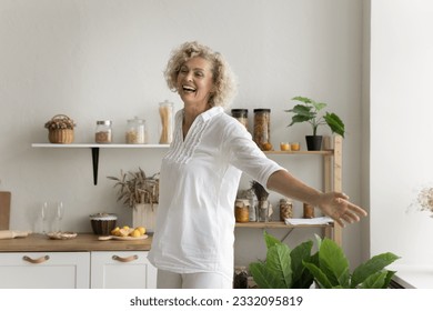 Cheerful pretty mature woman having fun at home kitchen, dancing with open arms, laughing, enjoying music, active leisure time, feeling happy, carefree, inspired - Powered by Shutterstock