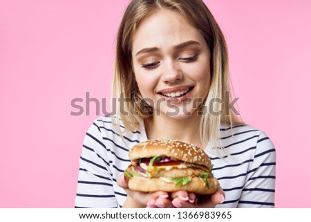 Cheerful pretty woman in a striped t-shirt hamburgers in her hands a diet pink background