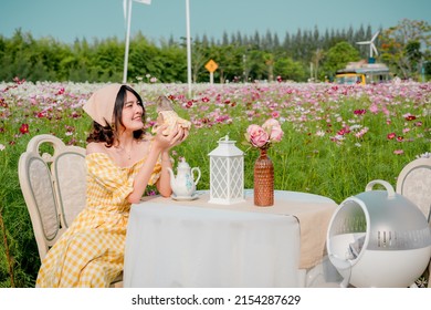 Cheerful Pretty Young Woman With Hair Tied By Handkerchief Holding And Kissing Cute Little Prairie Dog Sitting On Vintage Table Relaxing In Beautiful Flower Garden. Asian People.