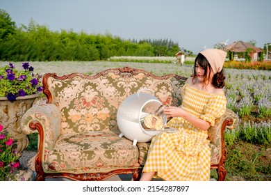 Cheerful Pretty Young Woman With Hair Tied By Handkerchief Holding And Hugging Cute Little Prairie Dog Sitting On Vintage Sofa Relaxing In Beautiful Flower Garden. Asian People.