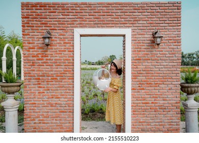 Cheerful pretty young woman with hair tied by handkerchief standing and holding carry box of her lovely Prairie dog pet in front of vintage red brick door in beautiful flower garden with blue sky.