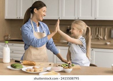 Cheerful proud mom teaching adorable little kid girl to cook, giving high five over table with ingredients for sandwiches, laughing, enjoying culinary, leisure, household activity with daughter - Powered by Shutterstock