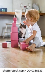 Cheerful redhead toddler arrangement pink cubes assembling tower educational Maria Montessori materials. Male kid playing self educational early development supplies toys sitting on floor at home