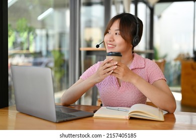 Cheerful And Relaxed Asian Young Online Teacher Taking A Break, Sipping Coffee In The Coffee Shop.