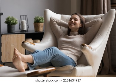 Cheerful relaxed beautiful 20s girl resting in comfortable armchair with closed eyes, peaceful smile, comfort, breathing fresh air. Smiling at good thoughts, laughing. Cozy home, relaxation concept