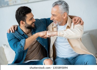 cheerful retired man fist bumping with happy bearded son at home 