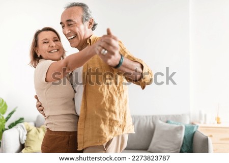 Cheerful retired spouses husband and wife dancing and laughing in living room, happy romantic couple enjoying slow dance, celebrating anniversary at home