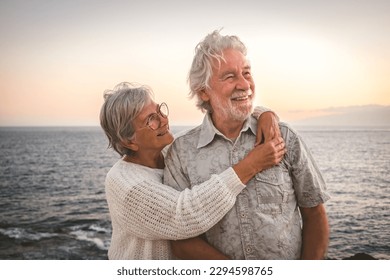 Cheerful romantic senior couple embraced at the sea at sunset light - old people outdoors enjoying vacations or retirement together - Powered by Shutterstock