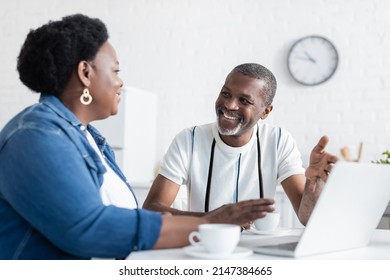 Cheerful Senior African American Couple Looking At Each Other Near Laptop