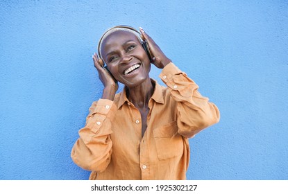 Cheerful senior african woman wearing headphones and dancing to playlist music