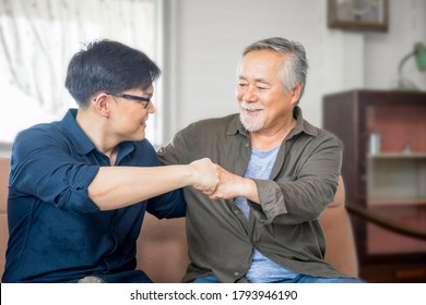 Cheerful Senior Asian Father And Middle Aged Son Fists Bumping, Mature Aged Dad And Millennial Man Sitting On Couch In Living Room At Home, Happiness Asian Family Concepts