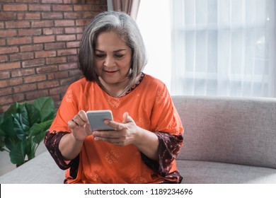 Cheerful Senior Asian Woman Using Her Smart Phone At Home