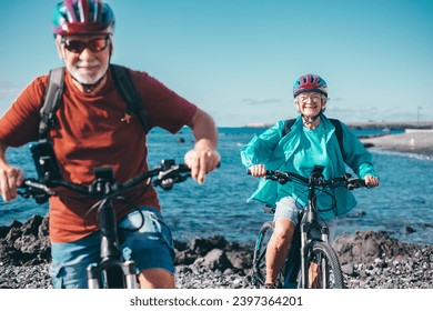 Cheerful senior couple enjoying riding bikes together at sea to be fit and healthy. Active seniors wearing helmets having fun training in outdoors. Authentic elderly retired life concept - Powered by Shutterstock