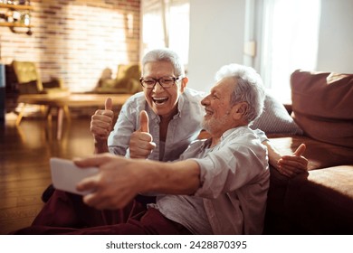 Cheerful senior couple giving thumbs up and taking a selfie at home - Powered by Shutterstock