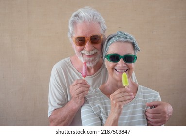 Cheerful Senior Couple Holding A Colored Popsicle Stick Looking At Camera, Happy Retirees Enjoying Retirement Eating A Fresh Popsicle