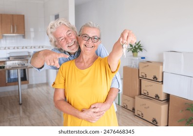 Cheerful senior couple hug enjoys moving into a new home, surrounded by moving boxes in an empty room. woman holding house keys, elderly retirees excited for their new beginning - Powered by Shutterstock