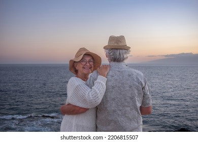 Cheerful Senior Couple Hugging At The Beach Standing Face The Sea At Sunset Light. Horizon Over Water