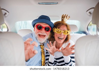 Cheerful Senior Couple With Party Accessories Sitting In Car, Having Fun.