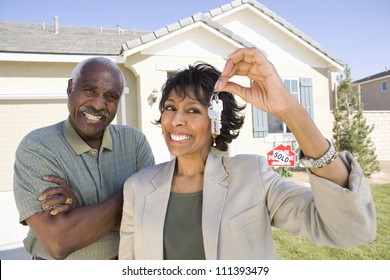 Cheerful Senior Couple Standing In Front Of House For Sale With Key