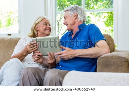 Cheerful senior couple using digital tablet while sitting in living room at home
